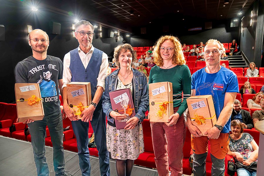 Gruppenbild der fünf Slammerinnen und Slamer des Science Slams 2023 auf der Bühne des Spremberger Spreekinos. Alle Teilnehmendes halten Präsente in den Händen und die Siegerin hat zusätzlich ein gläsernes Mikrophone als Trophäe erhalten.